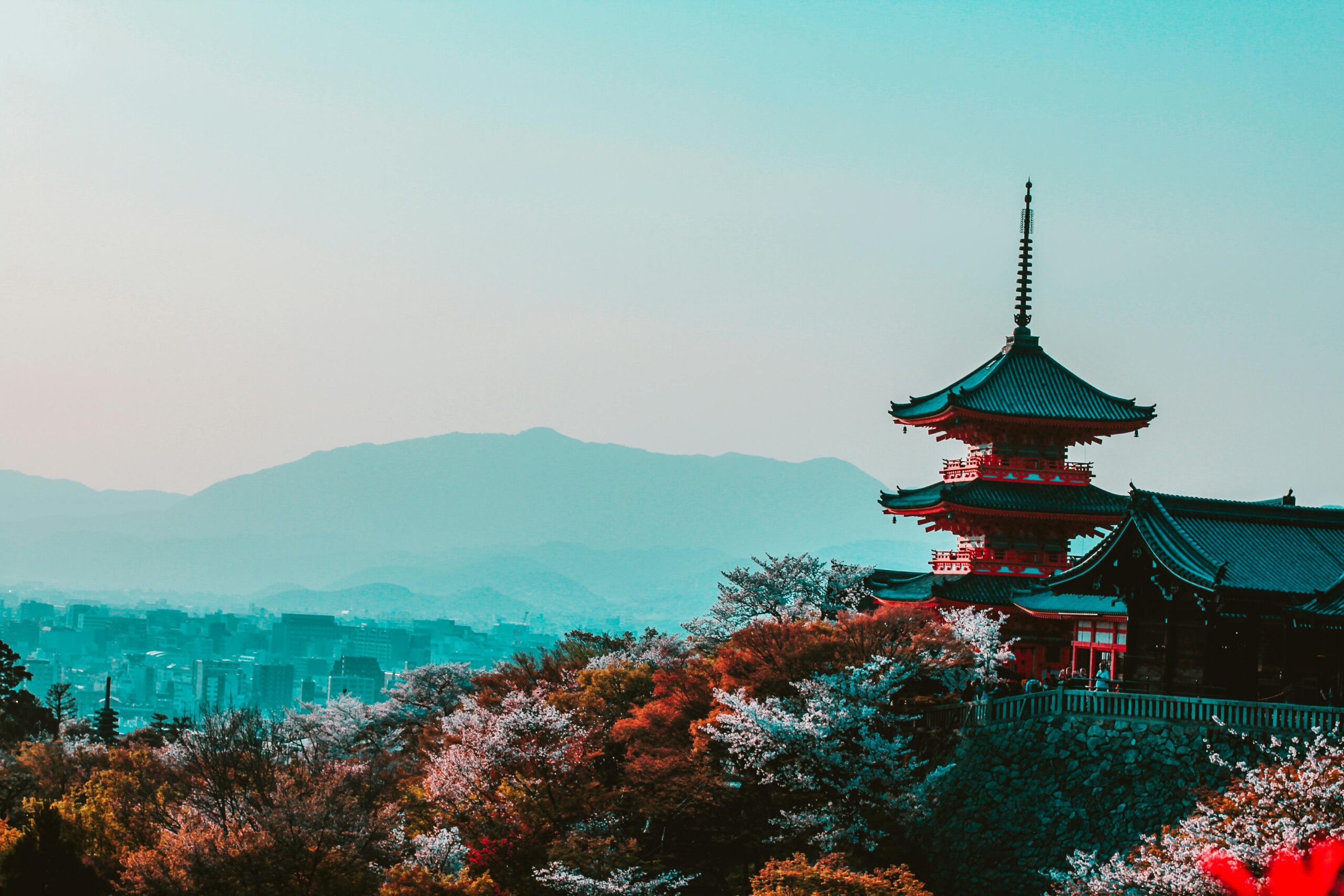 View of Kiyomizu-dera Temple in Kyoto, Japan, with a traditional pagoda, cherry blossoms, and mountains in the background.